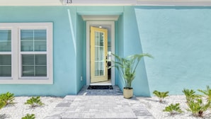 Un edificio de color azul claro, con el número 13 sobre la entrada, una puerta de vidrio y una pequeña planta en maceta al frente.