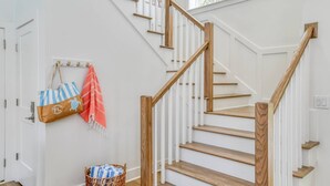 Una escalera con escalones de madera y barandillas blancas, una cesta de mimbre con una toalla a rayas, y un bolso colgado en un gancho.
