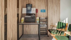 Un área de recepción con un muro de madera, un mostrador de registro, una computadora, un teléfono rojo y sillas verdes.