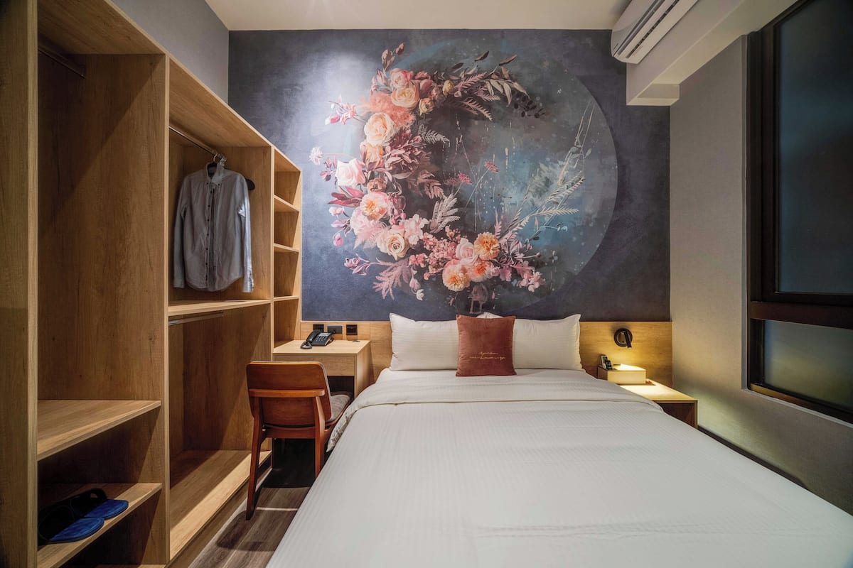 A hotel room with a large bed, a wooden wardrobe, a desk with a chair, and a wall mural.