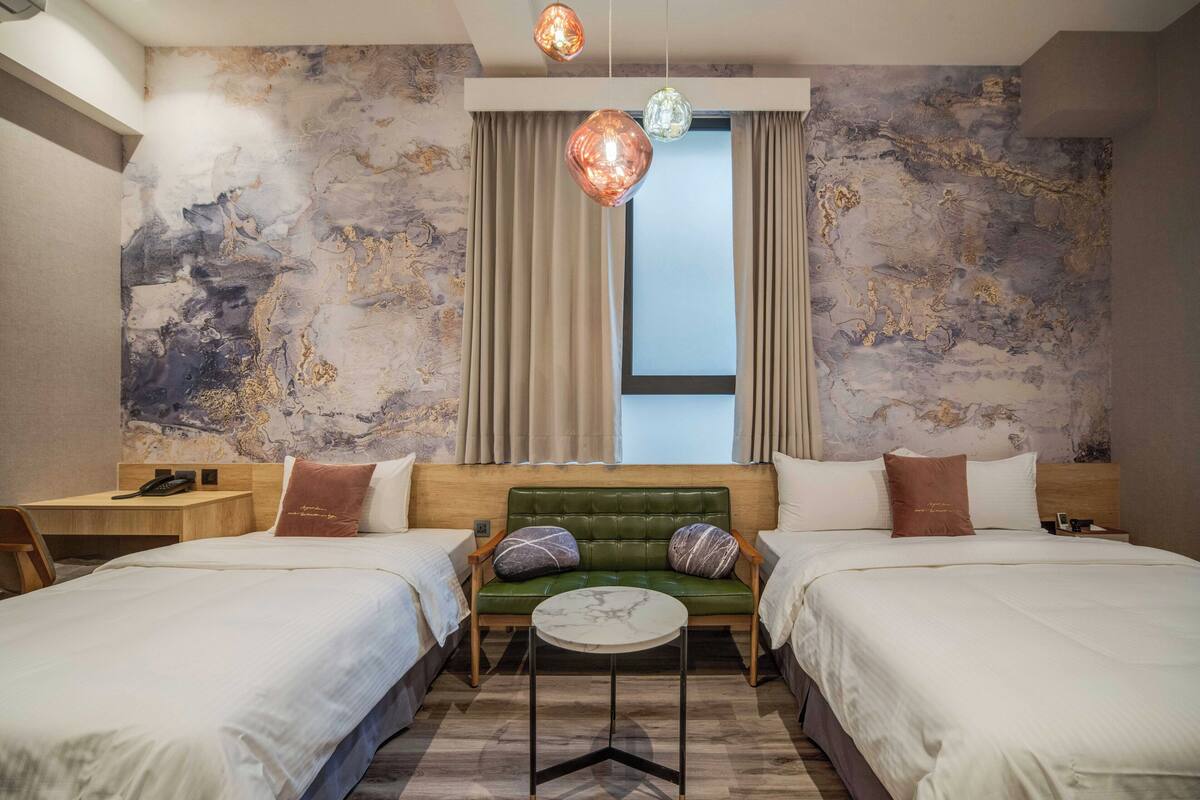 A hotel room with two beds, a green sofa, a small round table, and a marble-patterned wall.