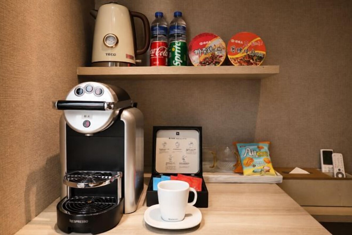 A kitchenette with a coffee maker, a kettle, and a cup on a table.