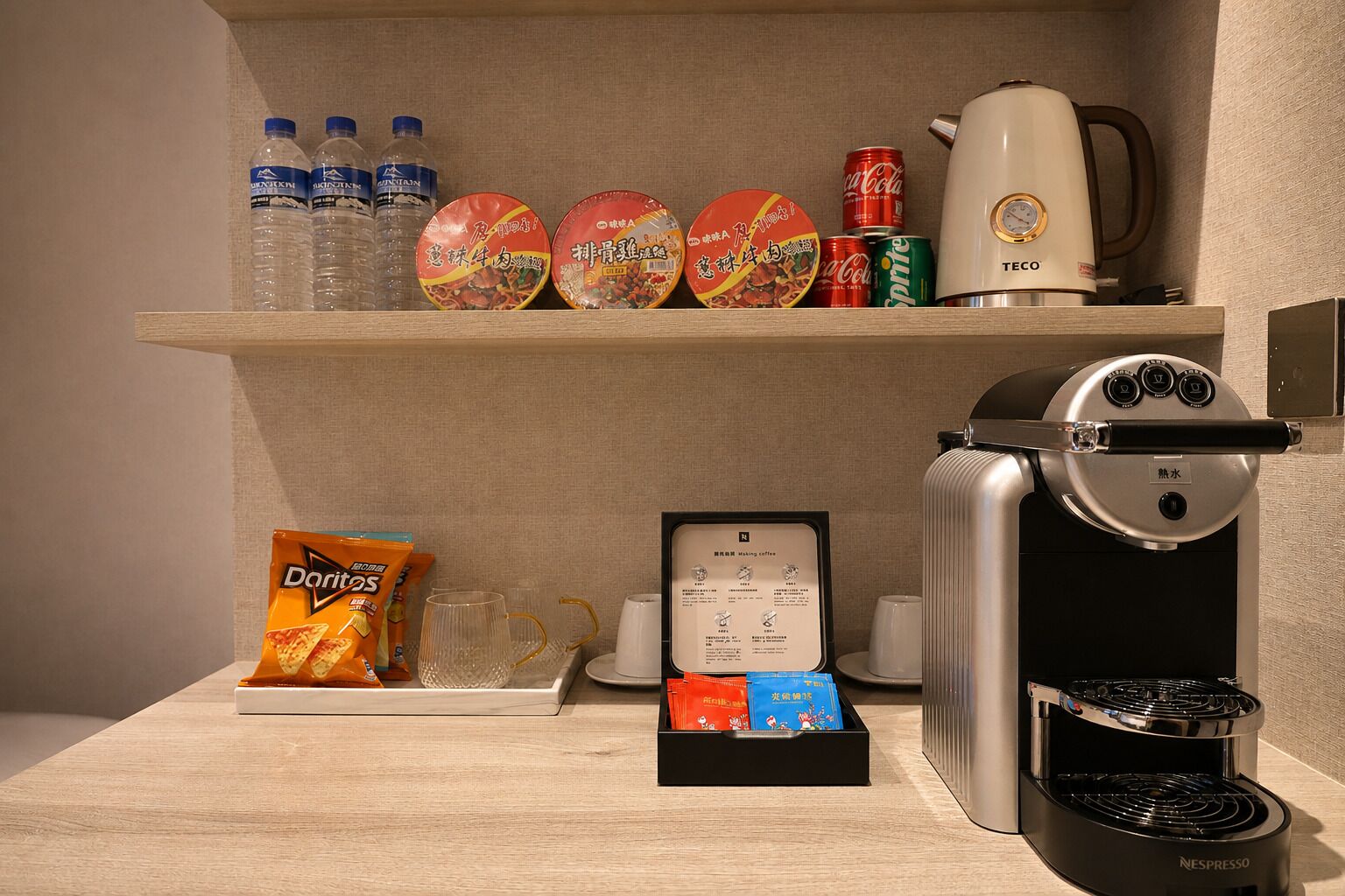 A hotel room's breakfast bar with a coffee machine, snacks, and bottled water.