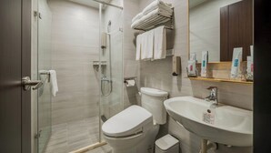Un baño moderno con ducha de vidrio, inodoro, lavamanos y espejo.