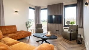 Un salon moderne comprenant un canapé, deux fauteuils, une table basse, un téléviseur et de grandes fenêtres avec des rideaux.