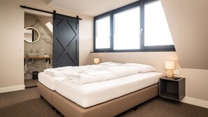 Une chambre à coucher moderne avec un lit, une salle de bain dotée d’un lavabo et d’un miroir, et une grande fenêtre.
