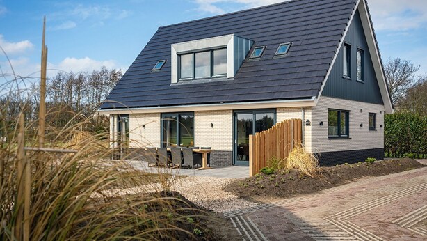 Une maison moderne avec un toit en pente, de grandes fenêtres et une allée pavée.
