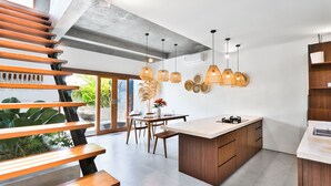 A modern kitchen with a central island, wooden staircase, and pendant lighting. - Octo 6 Villa by Betterplace (Canggu)