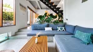 A modern living room with a grey sofa, wooden coffee table, and a staircase with a black railing. - Octo 6 Villa by Betterplace (Canggu)