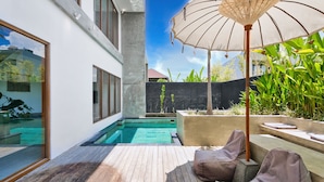 A modern outdoor pool area with a wooden deck, a lounge chair, and a large umbrella. - Octo 6 Villa by Betterplace (Canggu)
