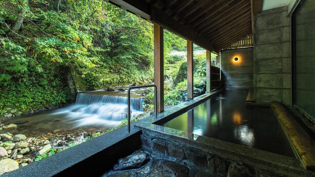 A hot spring area with a waterfall, stone steps, and a wooden ceiling.