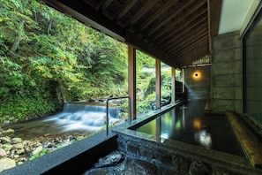 A hot spring area with a waterfall, stone steps, and a wooden ceiling.