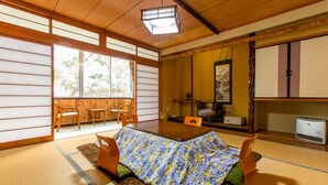 A traditional Japanese room with tatami flooring, a low table with a floral tablecloth, and a television.