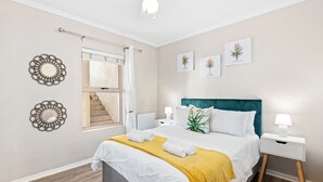 A neatly arranged bedroom with a bed, bedside tables, a ceiling fan, and wall art. - Bougain Villa CB206 (Cape Town)