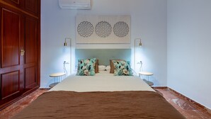 A bedroom with a large bed, wooden wardrobe, wall-mounted air conditioner, decorative wall art, and bedside lamps. - Pastor y Landero 17. 2-bedrooms. Arenal area (Sevilla)