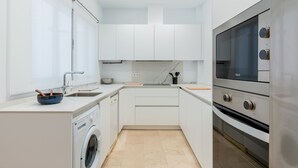 A modern kitchen with white cabinets, a built-in washing machine, a stainless steel oven, and a large window providing natural light. - Pastor y Landero 17. 2-bedrooms. Arenal area (Sevilla)