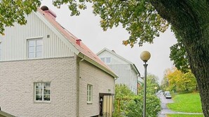 Un immeuble résidentiel à la façade en briques, doté d’un toit rouge et d’un petit jardin devant, agrémenté d’une clôture et d’un lampadaire.