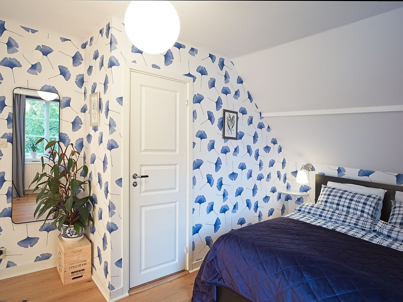 A bedroom with a bed, a bedside table, a lamp, a mirror, and a door.