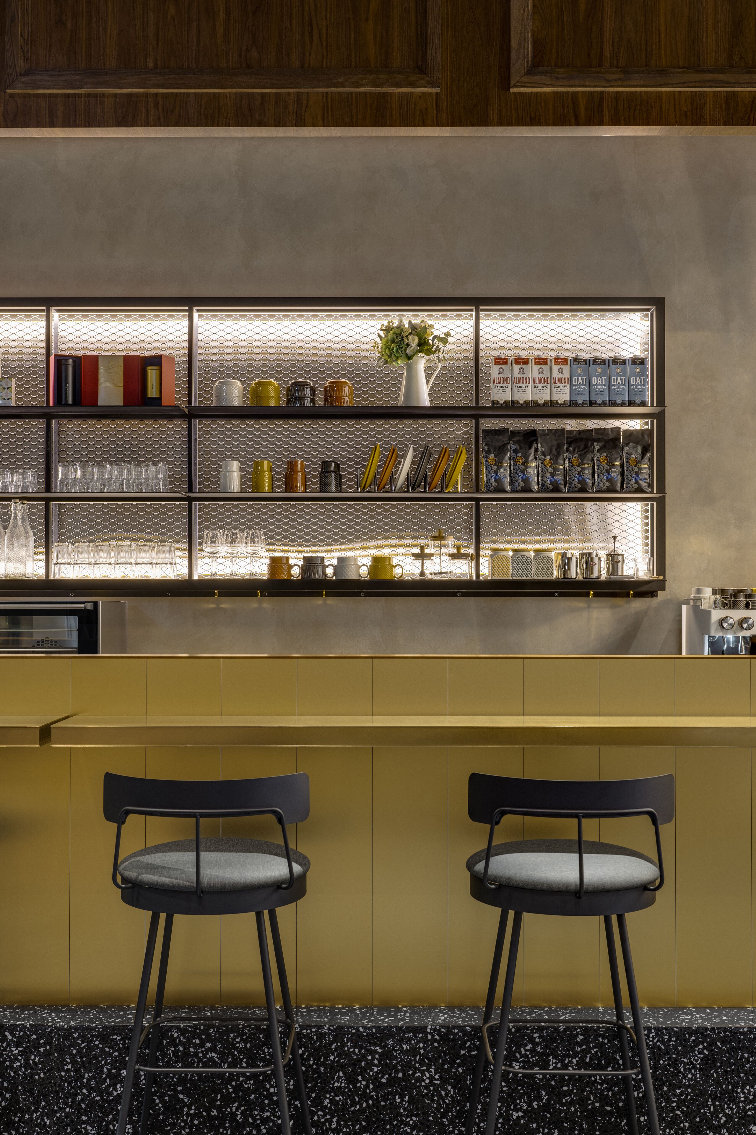 A bar area with a metal shelf displaying various items, two black chairs, and a yellow counter.