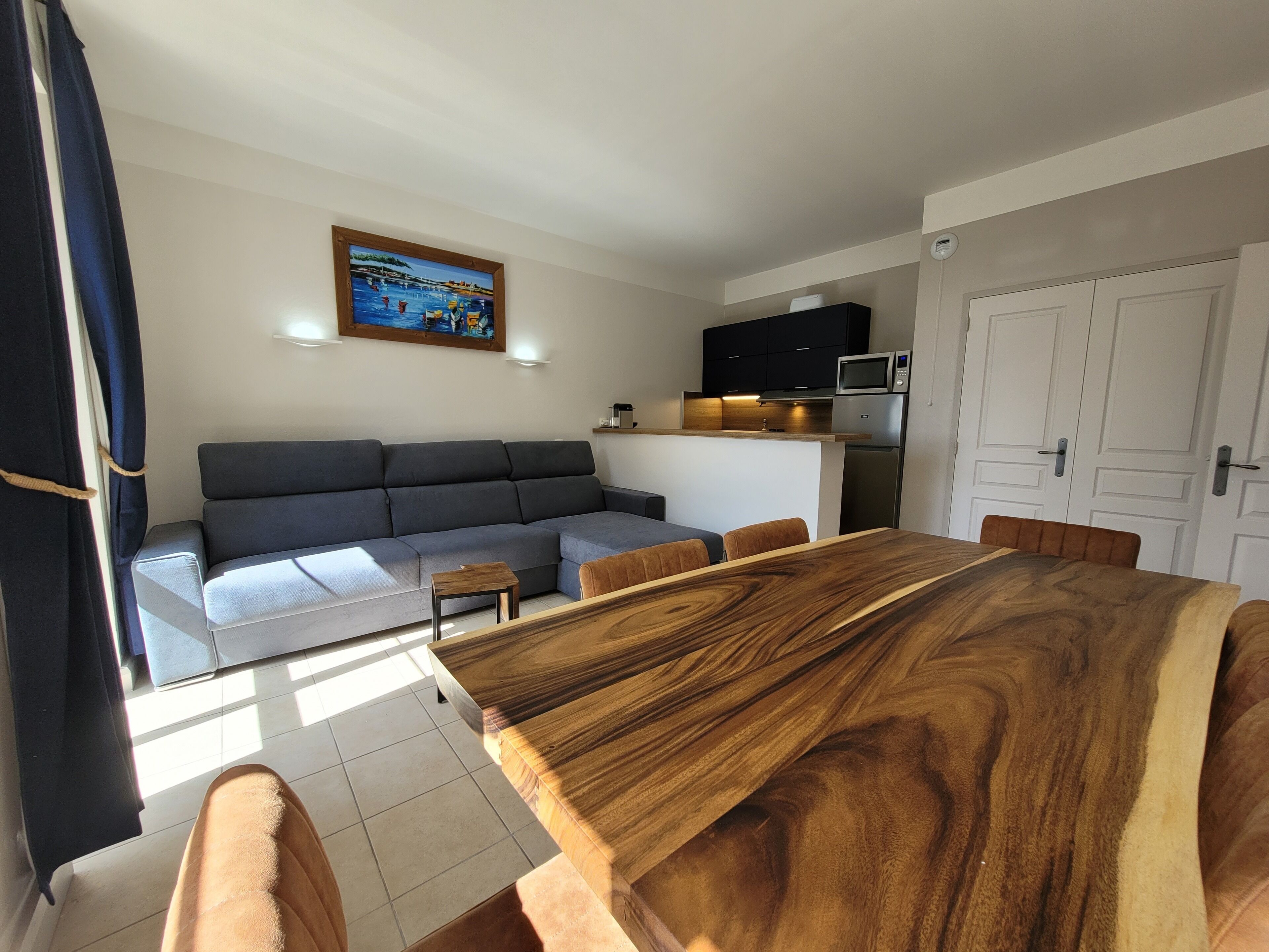 Een moderne woonkamer met een hoekbank, een houten eettafel en een keuken voorzien van een magnetron en kastjes.