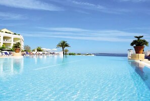 Une magnifique piscine à débordement d’un bleu profond, agrémentée de chaises longues et de palmiers, avec une vue imprenable sur la mer.