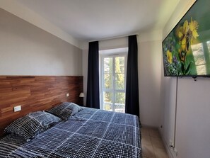 Une chambre à coucher avec une tête de lit en bois, un lit recouvert d’une couvre-lit à motifs, une fenêtre avec des rideaux et un tableau représentant des fleurs accroché au mur.
