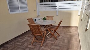 Eine Terrasse mit Tisch und vier Stühlen, einem Blumentopf und einem weißen Zaun.