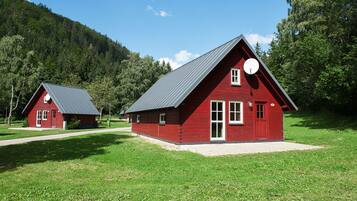 Due cabine di legno rosse con tetti spioventi, immerse in un prato con una collina boscosa sullo sfondo.