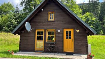 A wooden cabin with a yellow door and windows, a satellite dish, and a number '11' sign.