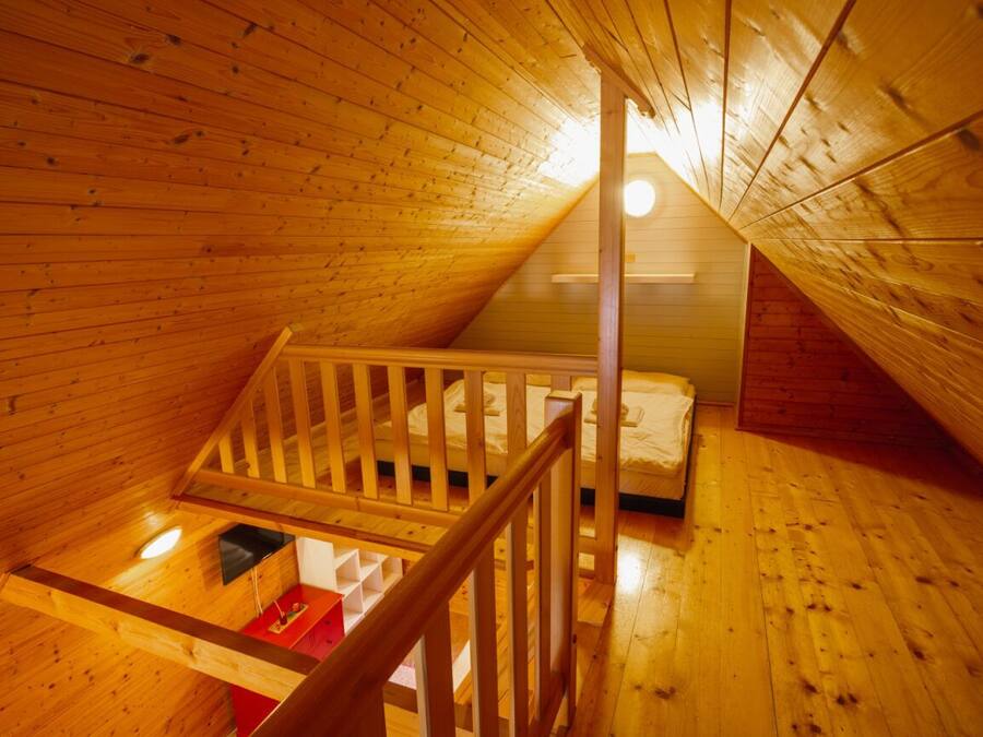 A wooden interior with a sloped ceiling, a wooden staircase, and a bed.