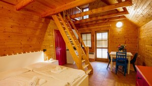 A wooden cabin bedroom with a bed, a desk, a chair, a red dresser, and a staircase. - Base Camp Medvědín (Spindleruv Mlyn)