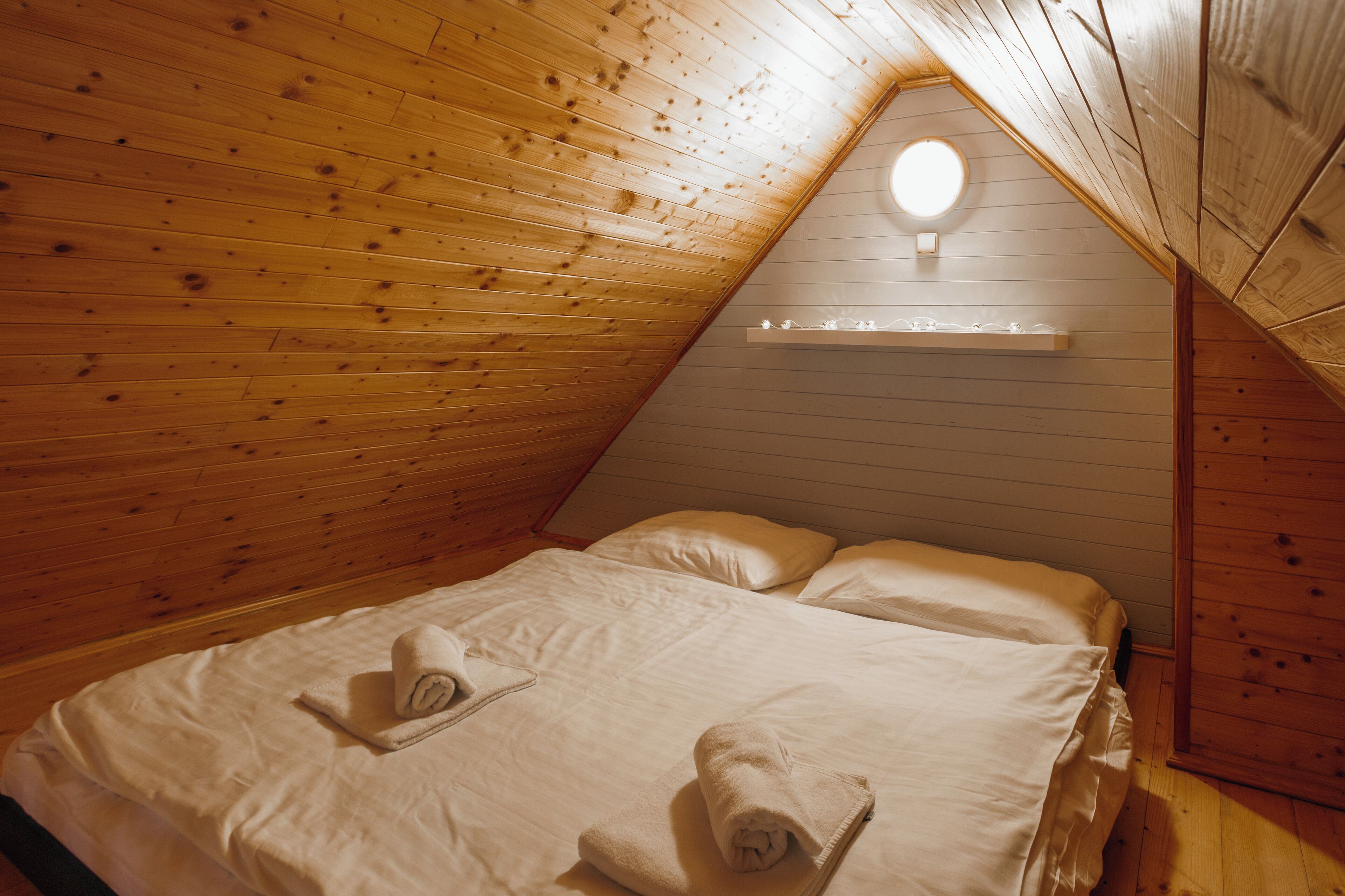 Una habitación acogedora con paneles de madera, una cama, dos almohadas y una lámpara fijada a la pared.