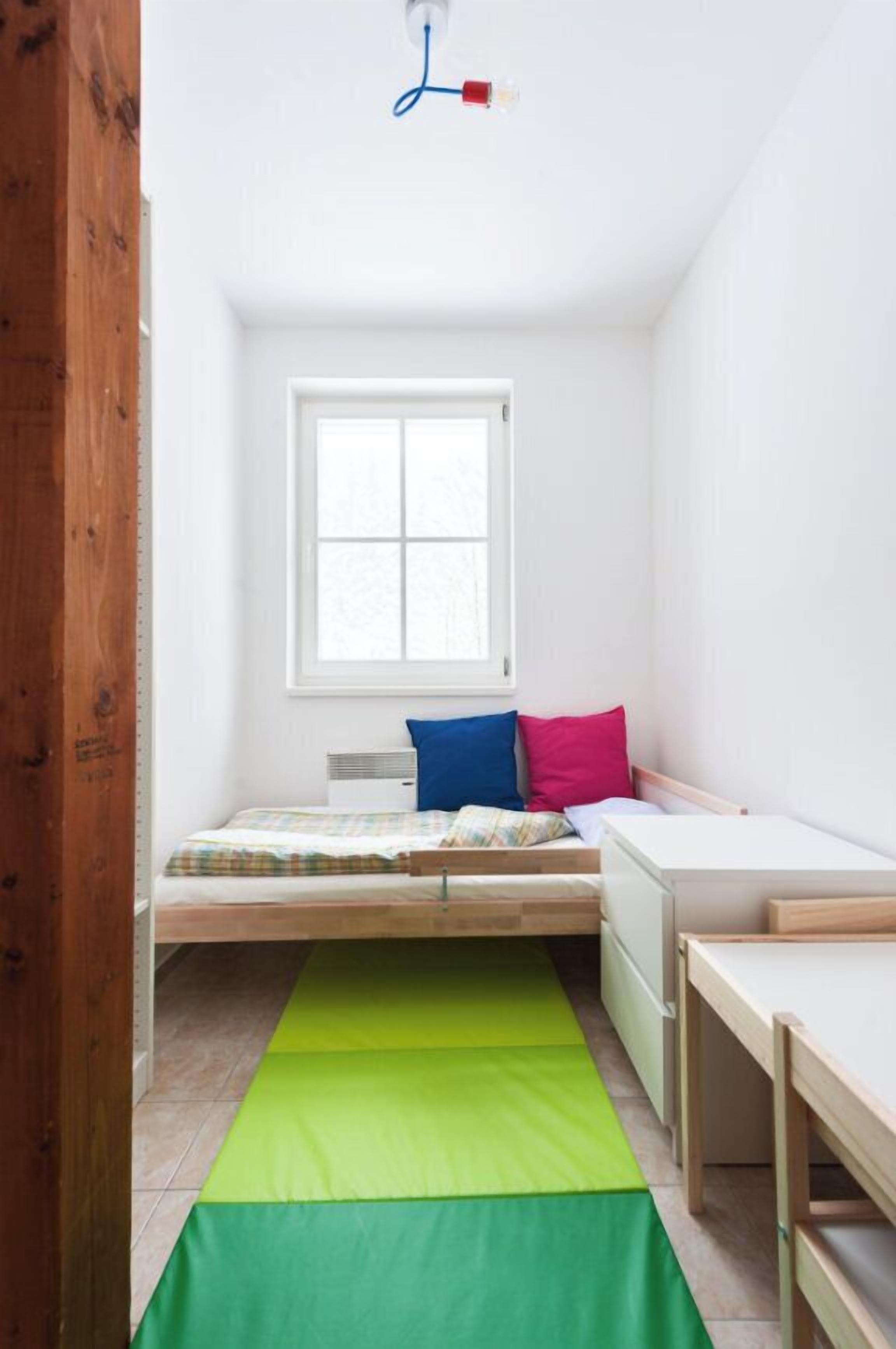 A small, bright room with a bed, a window, and a desk.