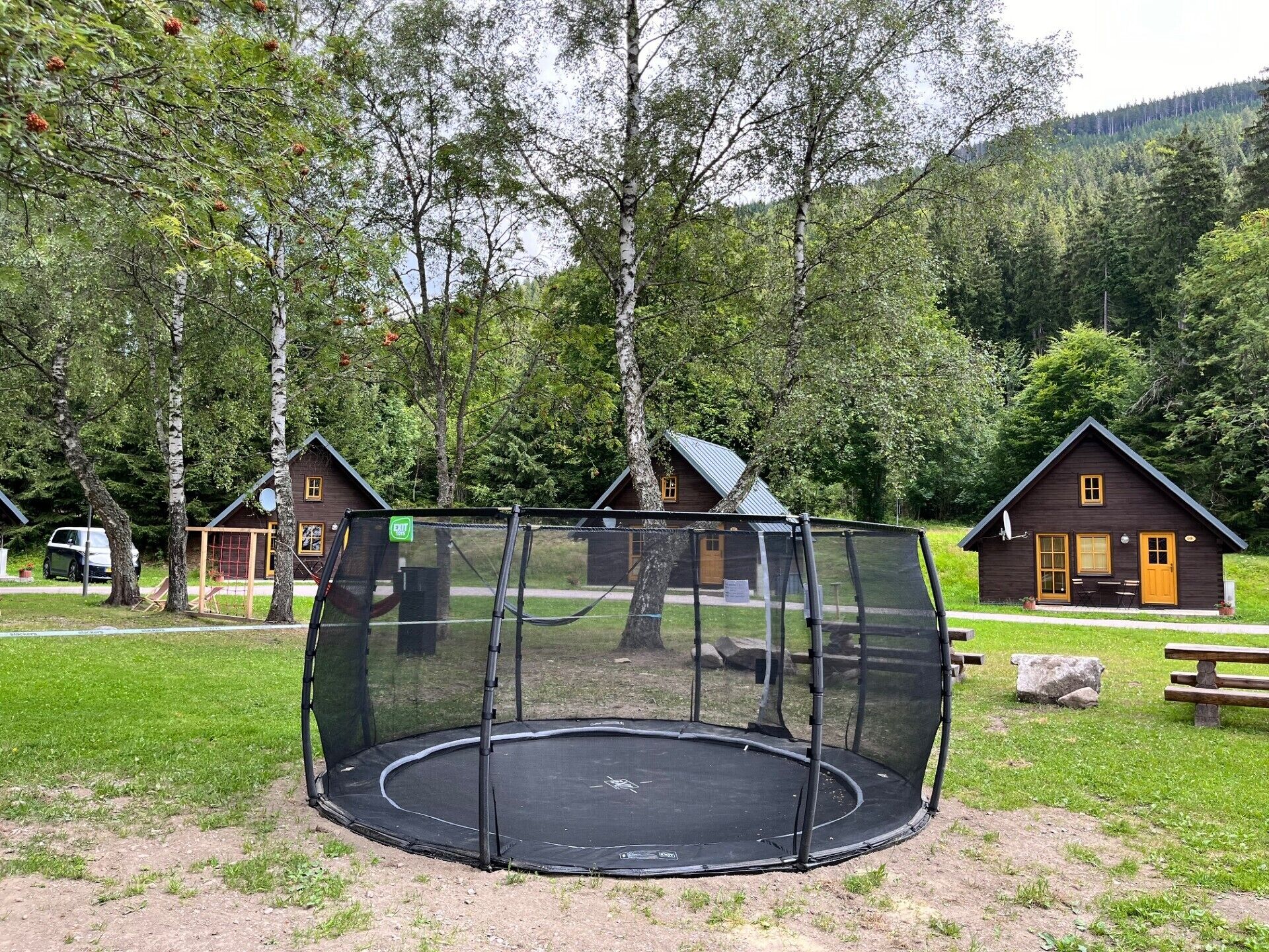 A trampoline in a wooded area with cabins in the background.