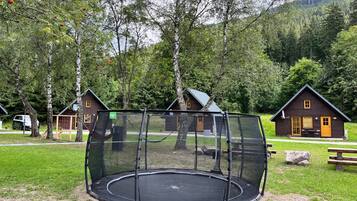 A trampoline in a wooded area with cabins in the background.