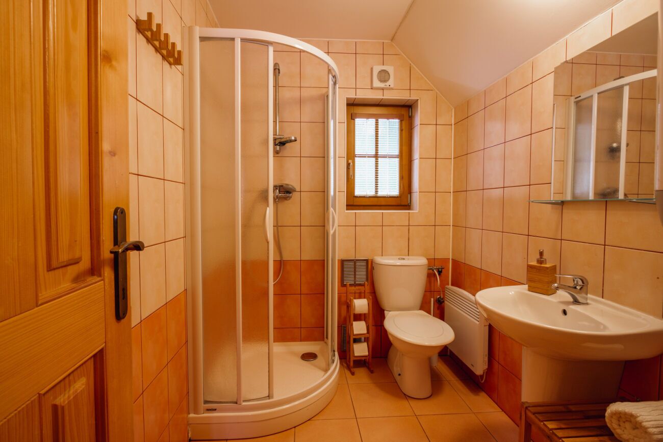 Et badeværelse med bruser, toilet, håndvask og et vindue.
