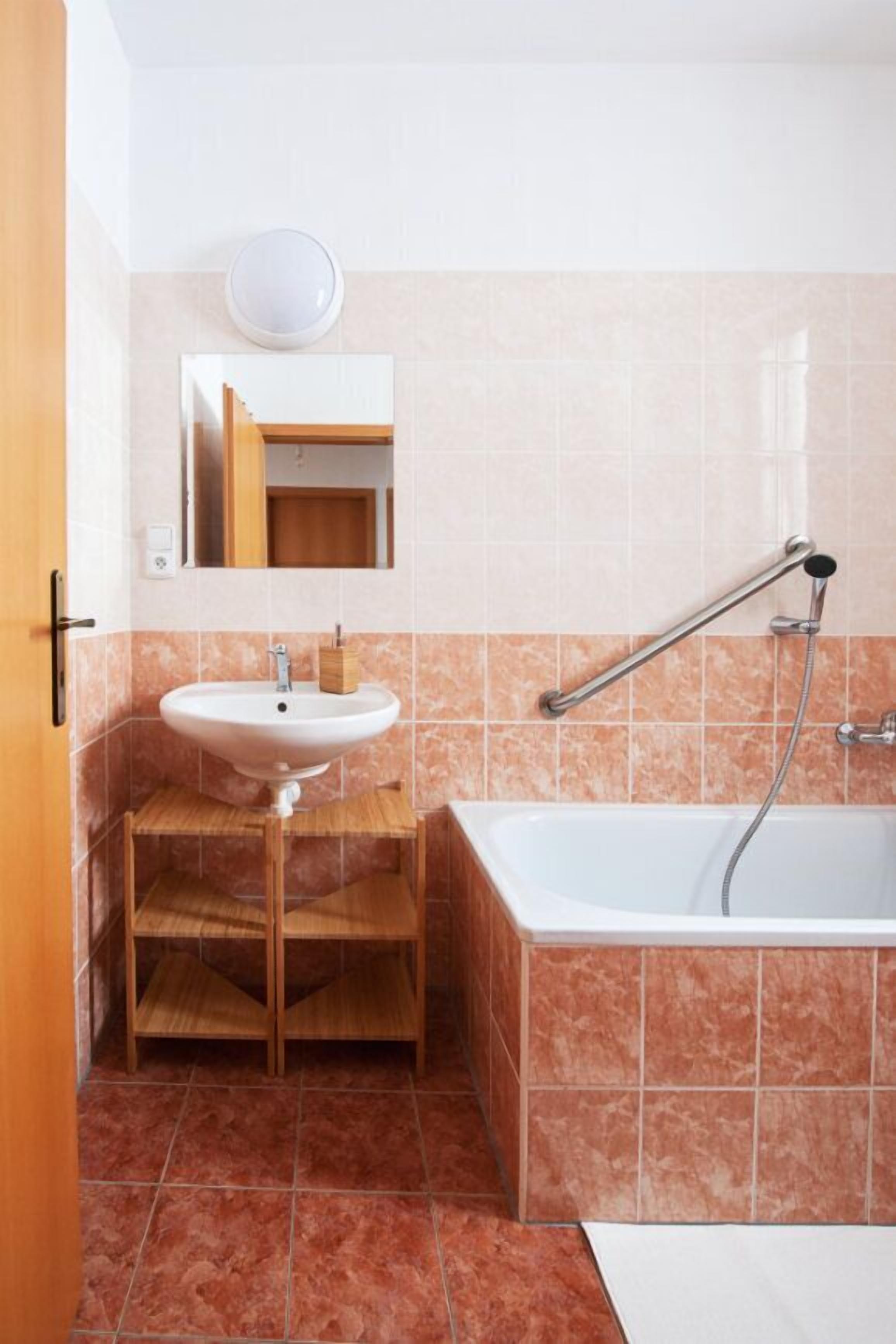 Un baño con lavamanos blanco, tocador de madera, espejo y bañera con ducha.