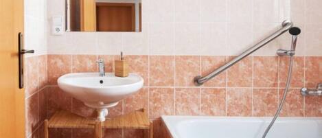A bathroom with a white sink, a wooden vanity, a mirror, and a bathtub with a showerhead.