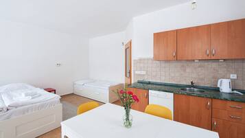 Een kleine hotelkamer met een bed, een tafeltje met een bloevas, een kitchenette met houten kastjes en een witte wasbak.