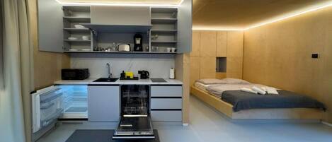 Een compacte slaapkamer met een geïntegreerde kitchenette, een bed en een klein werkplekje.