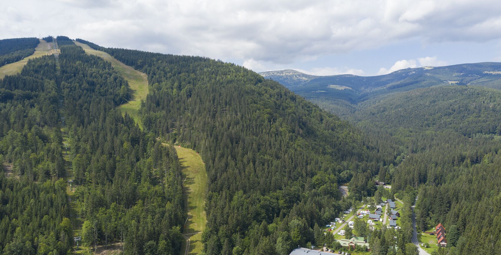 A mountainous area with a ski trail, dense forest, and a small village with houses and a road.