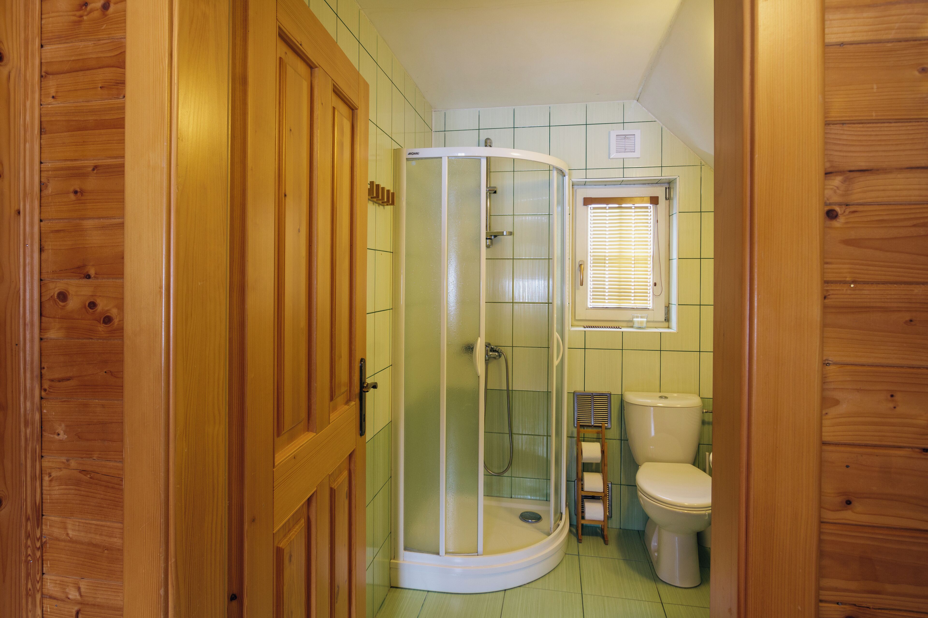 A bathroom with a shower enclosure, toilet, and a window with blinds.