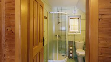A bathroom with a shower enclosure, toilet, and a window with blinds.