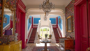 A grand hallway with a chandelier, a staircase, and a bed in the center. - Le Château du Breuil (Mazières-de-Touraine)