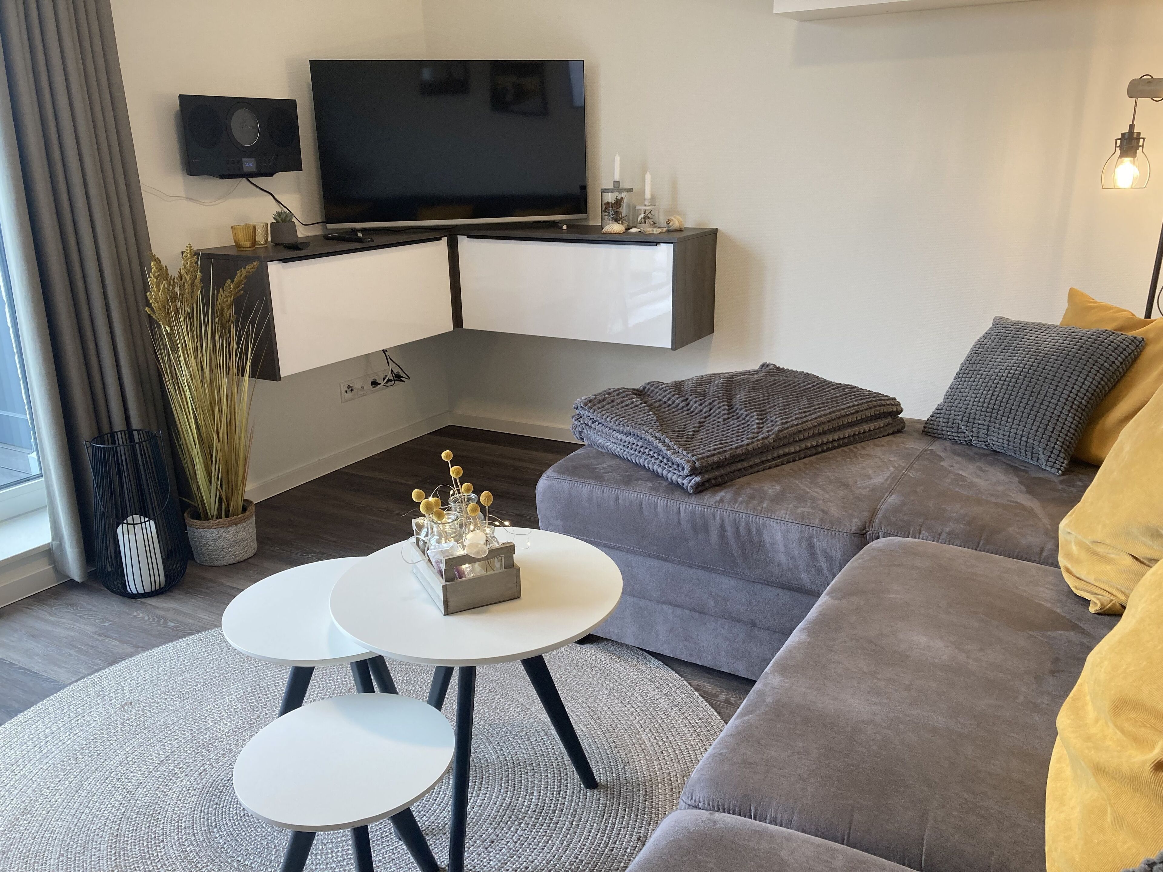 A modern living room with a grey sofa, a white coffee table, and a TV mounted on the wall.