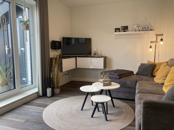 Un salon moderne avec un canapé gris, un téléviseur à écran plat, une petite table basse et un tapis rond.