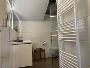 Une salle de bain moderne avec une douche à parois de verre, un tabouret en bois et un lavabo blanc.