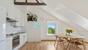 Een moderne keuken met witte kasten, een houten eettafel en uitzicht op groen door een raam.