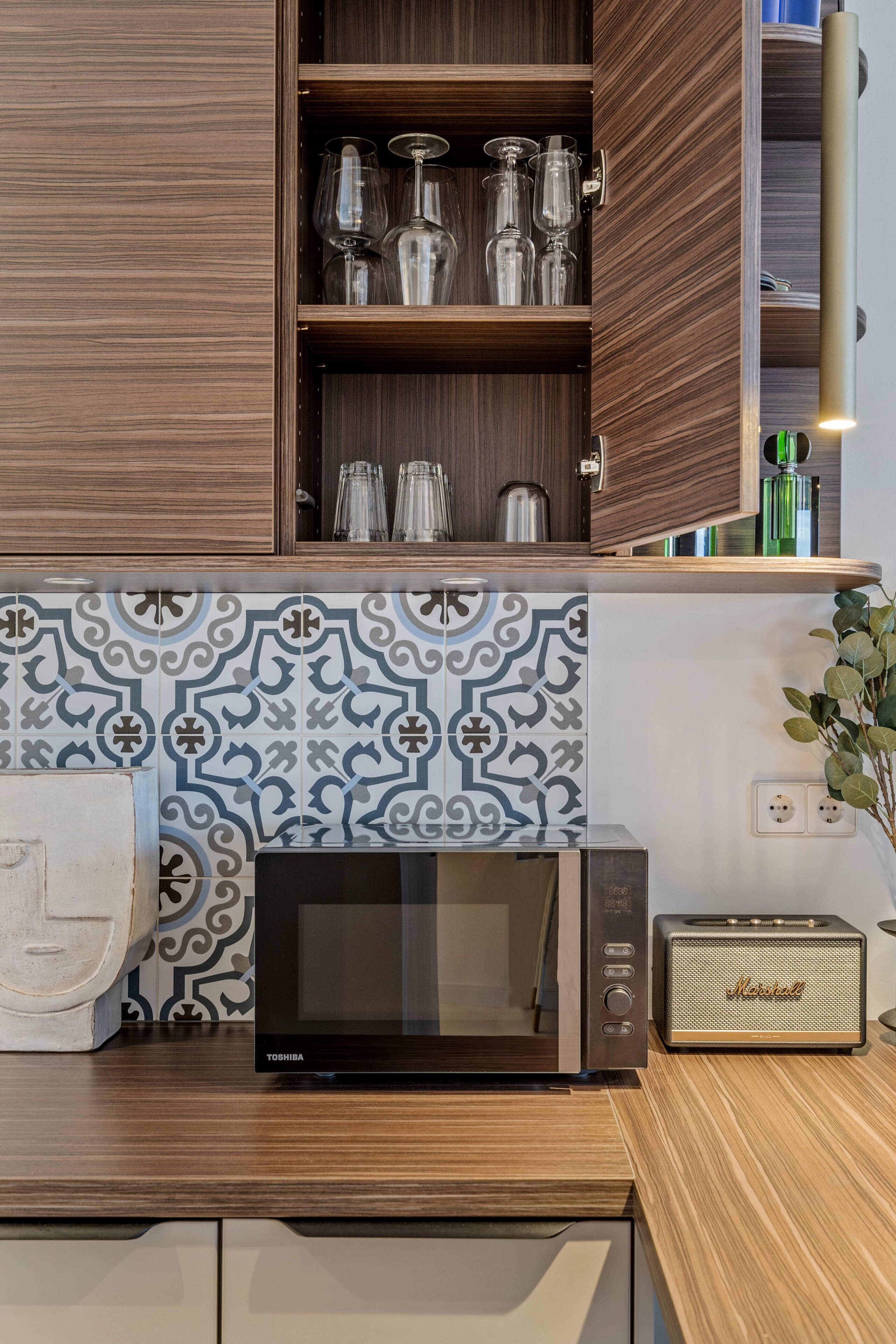 A kitchen with a microwave, a speaker, and a cabinet with glassware.