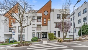 Un immeuble d’appartements moderne, doté d’un toit triangulaire imposant, d’une entrée centrale et d’une enseigne portant l’inscription « BLUES ».